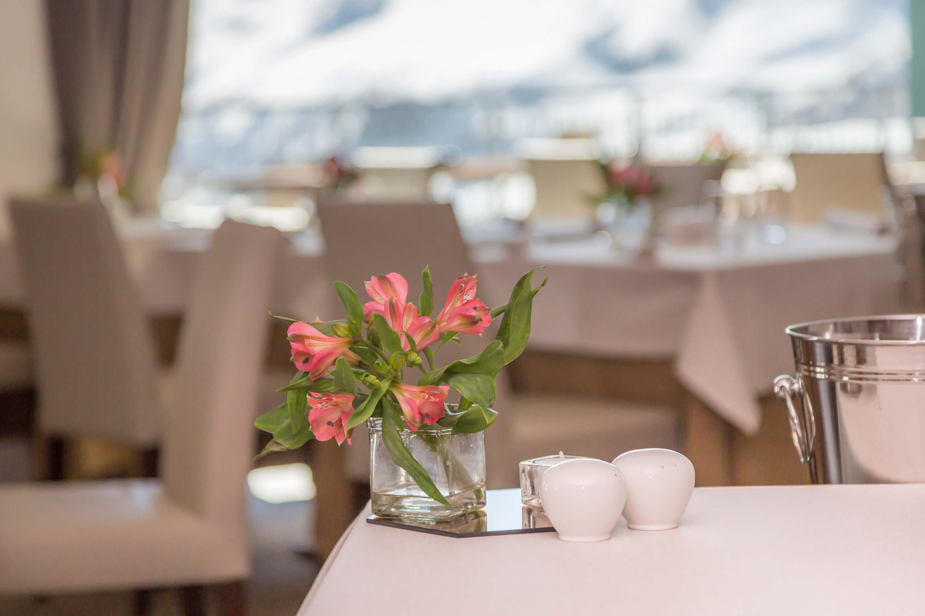 Elegant dining scene with a white tablecloth, pink flowers, salt and pepper shakers, and a silver wine bucket.